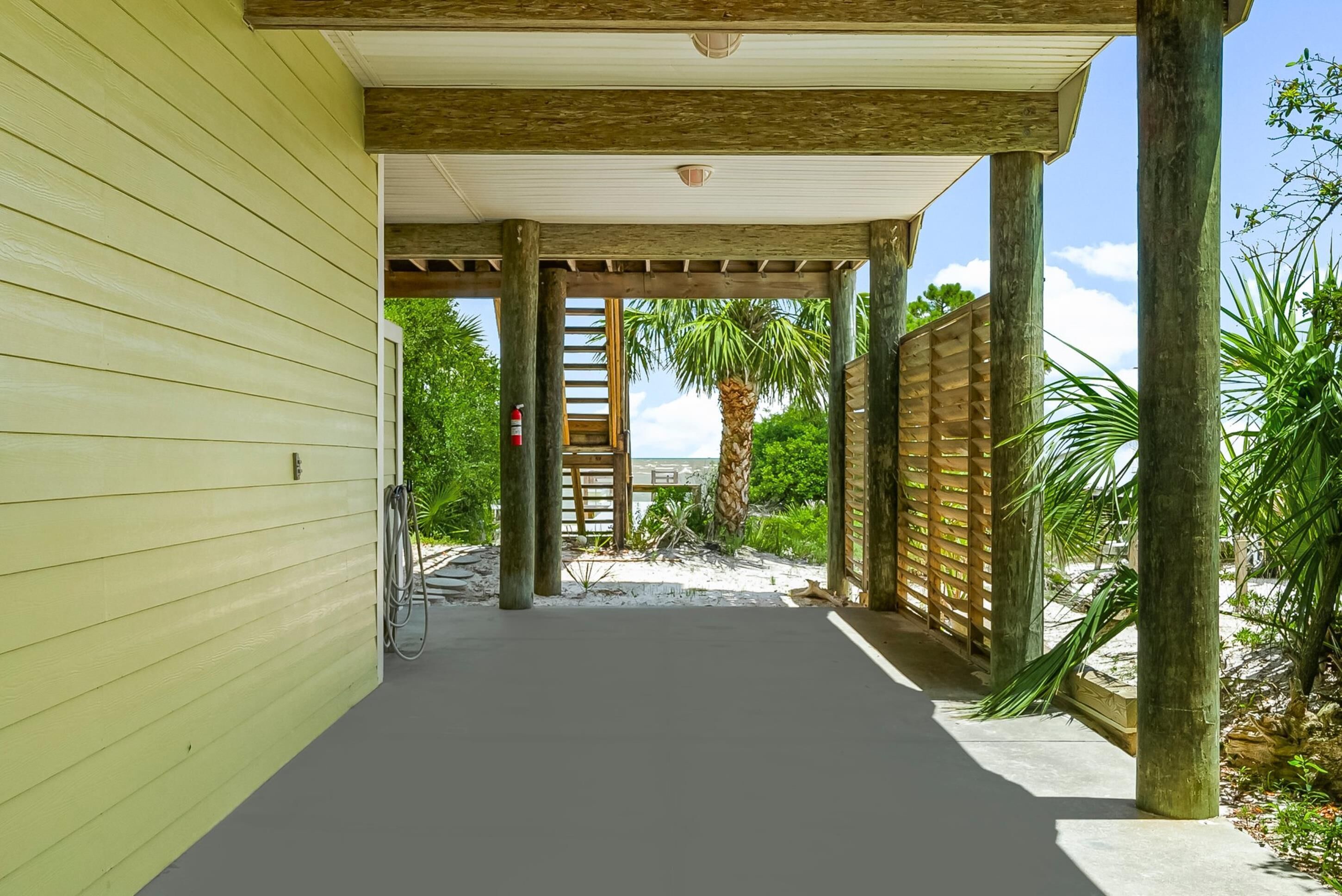 A covered walkway leading to a beach area with a wooden fence and palm trees.