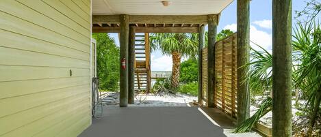 A covered walkway leading to a beach area with a wooden fence and palm trees.