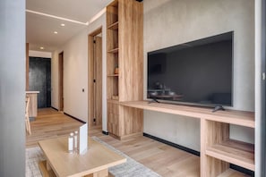 Een moderne woonkamer met een flatscreen televisie bevestigd aan een houten console, een eethoek met een houten tafel en stoelen, en een keuken in de achtergrond.