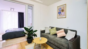 Una habitación moderna con una cama, un sofá gris, una mesita redonda y una planta en maceta.