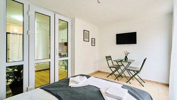 Habitación de hotel con cama, escritorio, silla, televisor y puerta corrediza de vidrio que da a un balcón.