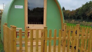 A green, dome-shaped building with a wooden door and a sign reading "Heron". - Green Dragon and Kitchen Pod - Sleeps 2 & Parking (Welshpool)