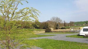 A gravel parking area with a white caravan parked on the right. - Green Dragon and Kitchen Pod - Sleeps 2 & Parking (Welshpool)