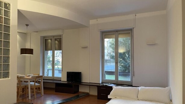 Une chambre à coucher comprenant un lit, un bureau avec une chaise, une télévision et de grandes fenêtres.