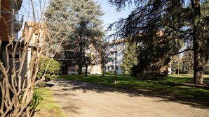 A paved driveway leading to a building with a grassy area and trees. - Accomodo MIT12 Trivano Linate  (Milan)