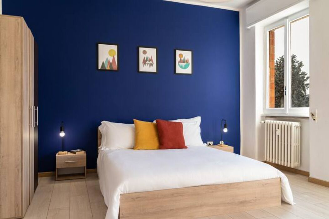 Un dormitorio con una cama, una mesita de noche, una ventana y tres cuadros en la pared.