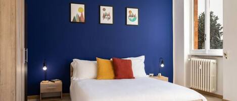 Un dormitorio con una cama, una mesita de noche, una ventana y tres cuadros en la pared.