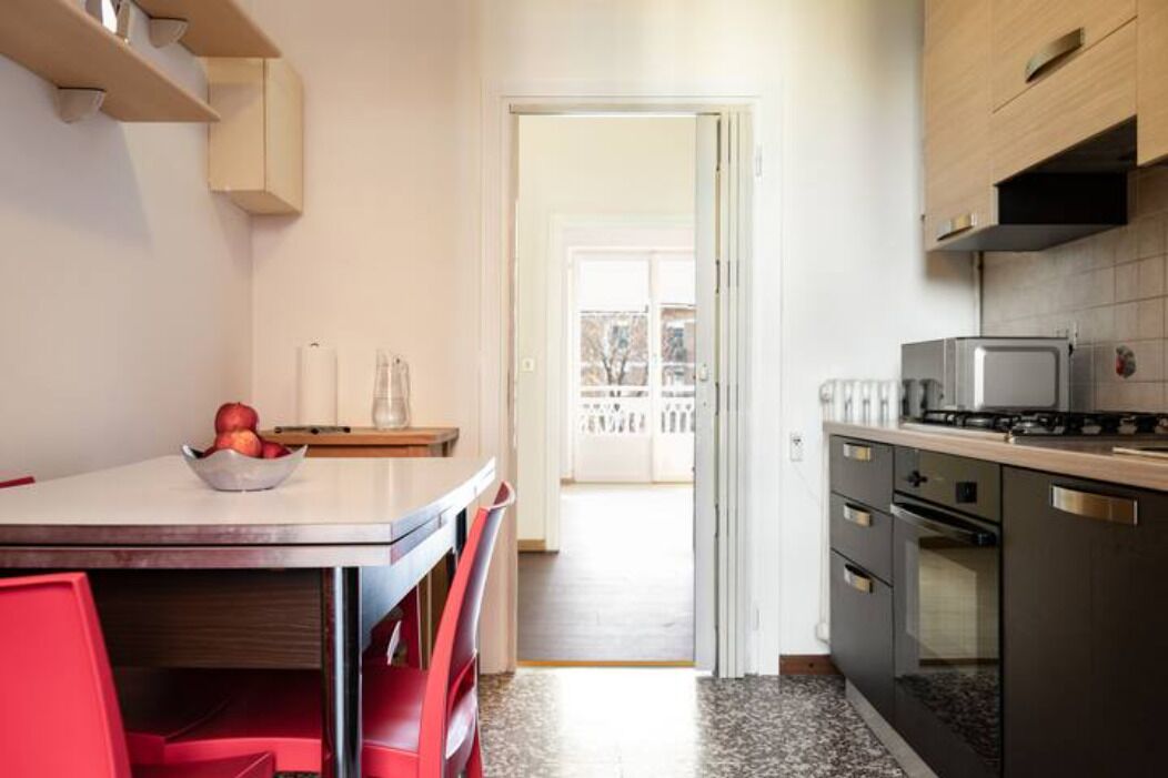 A kitchen with a dining table, chairs, a bowl of fruit, a stove, and an oven.