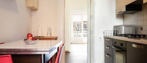 A kitchen with a dining table, chairs, a bowl of fruit, a stove, and an oven.