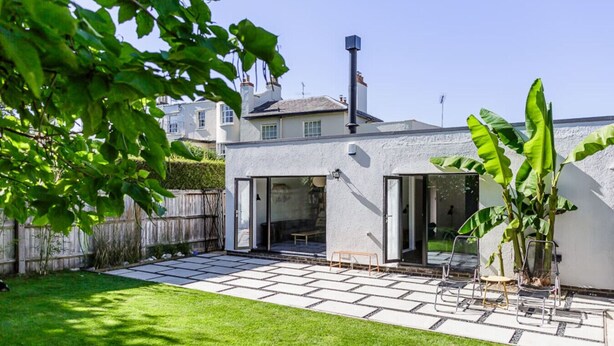 A modern house with a patio, a wooden fence, and a large tree. - Mid-Century Modern Style 1BD House w/ Large Garden (Gloucestershire)