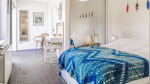A modern hotel room with a large bed, a desk, and a chair. There is a mirror on the wall and a door leading to another room. - Mid-Century Modern Style 1BD House w/ Large Garden (Gloucestershire)