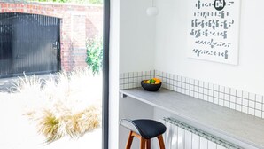 A modern kitchen with a white countertop, a black bowl of fruit, and a wooden stool. - Mid-Century Modern Style 1BD House w/ Large Garden (Gloucestershire)