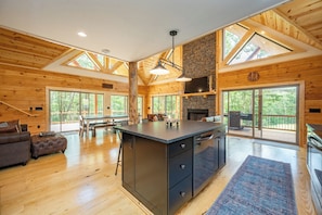 A spacious kitchen with a central island, wooden walls, large windows, and a fireplace.
