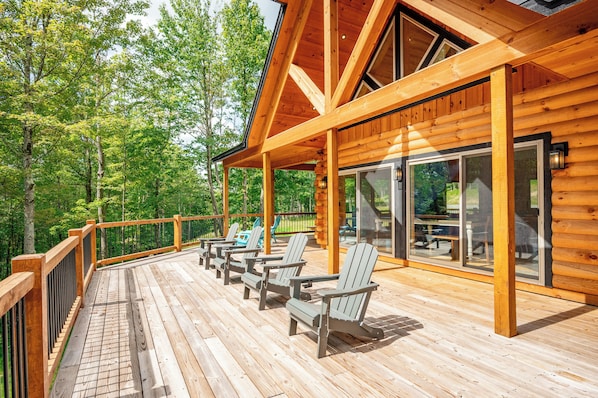 A wooden deck with Adirondack chairs and a glass door leading to a covered area.