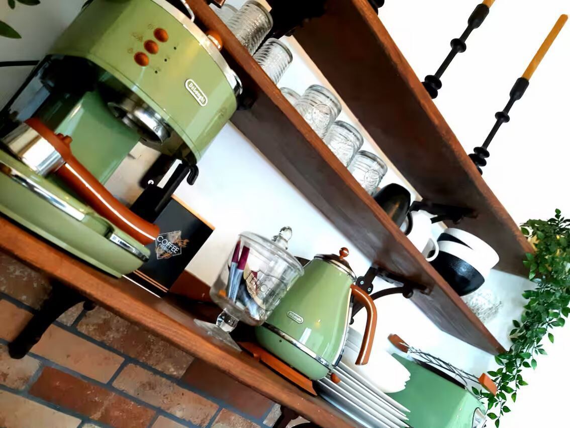 A kitchen with vintage green appliances, a coffee maker, and a shelf with jars.