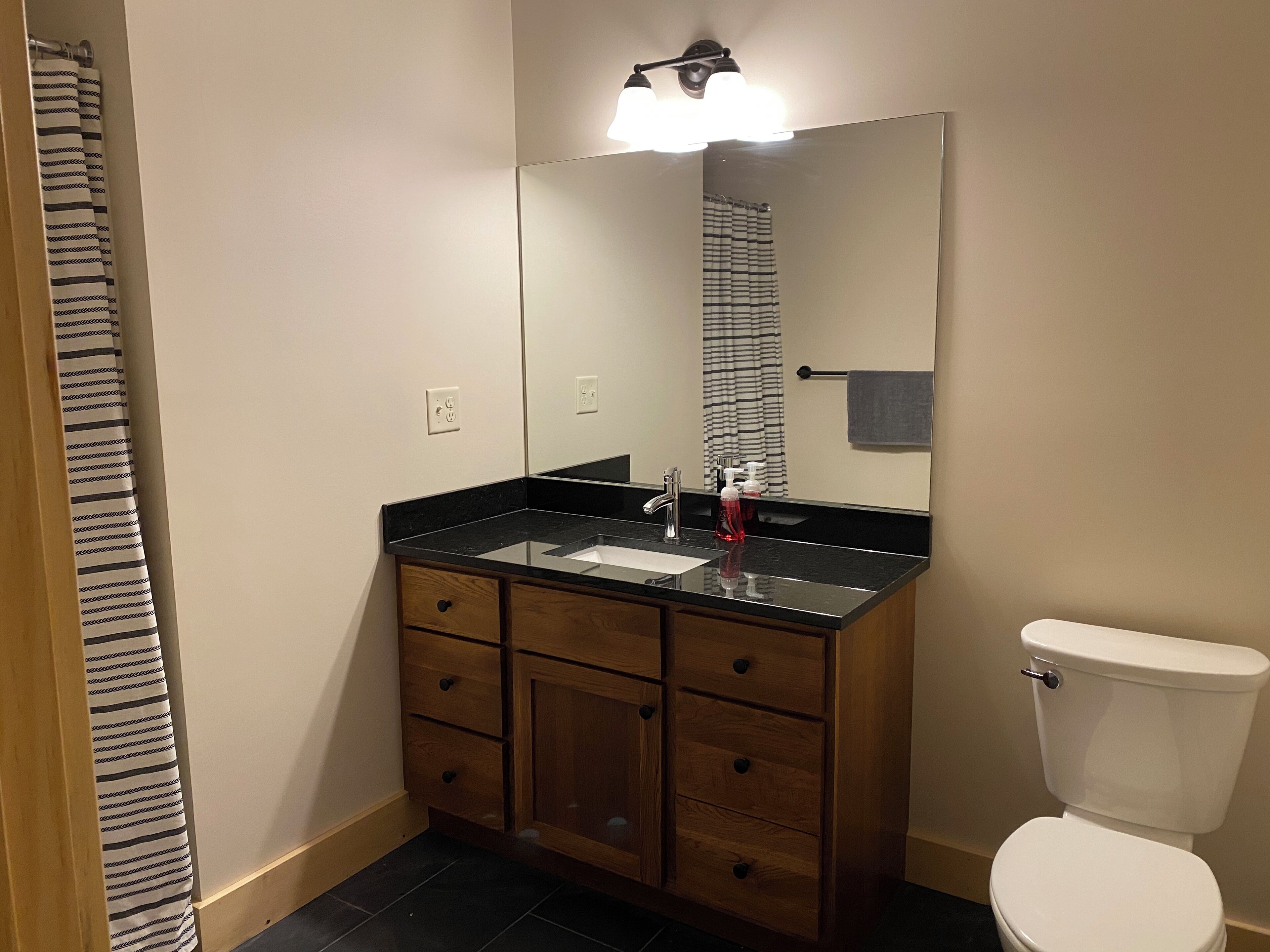 Ein Badezimmer mit schwarzem Waschtisch, einem Spiegel, Holzschränken und einer weißen Toilette.