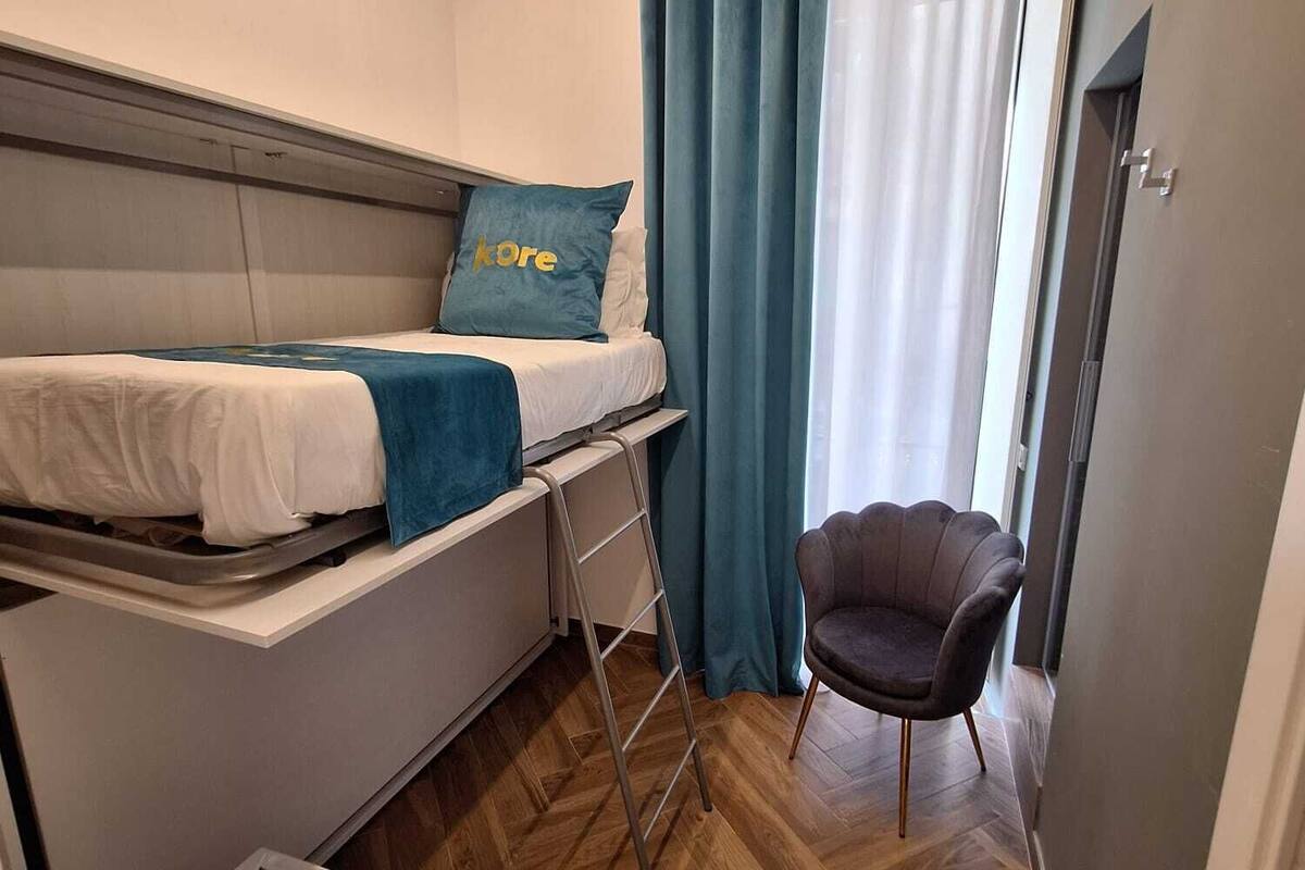 Una camera d'albergo compatta con un letto a castello, una scrivania, una sedia e un armadio.