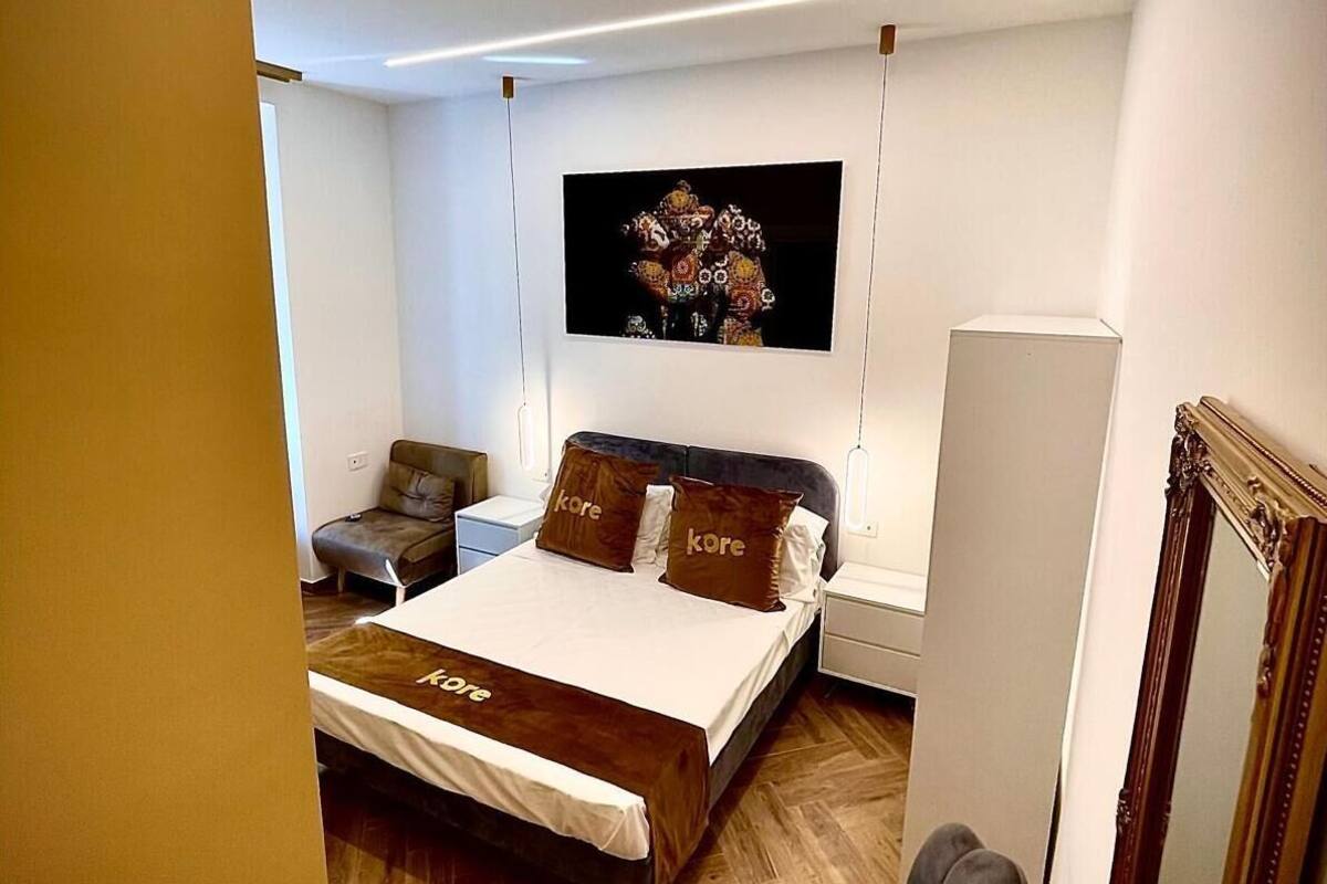 Camera da letto moderna con un letto grande, un comodino, una sedia, uno specchio e una TV a parete.
