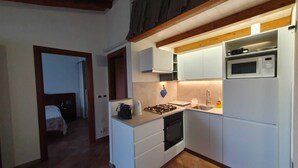Een kleine keuken met witte kastjes, een magnetron, een kookplaat en een spoelbak.