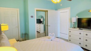 Une chambre à coucher comprenant un lit, un ventilateur de plafond, un téléviseur et une commode.