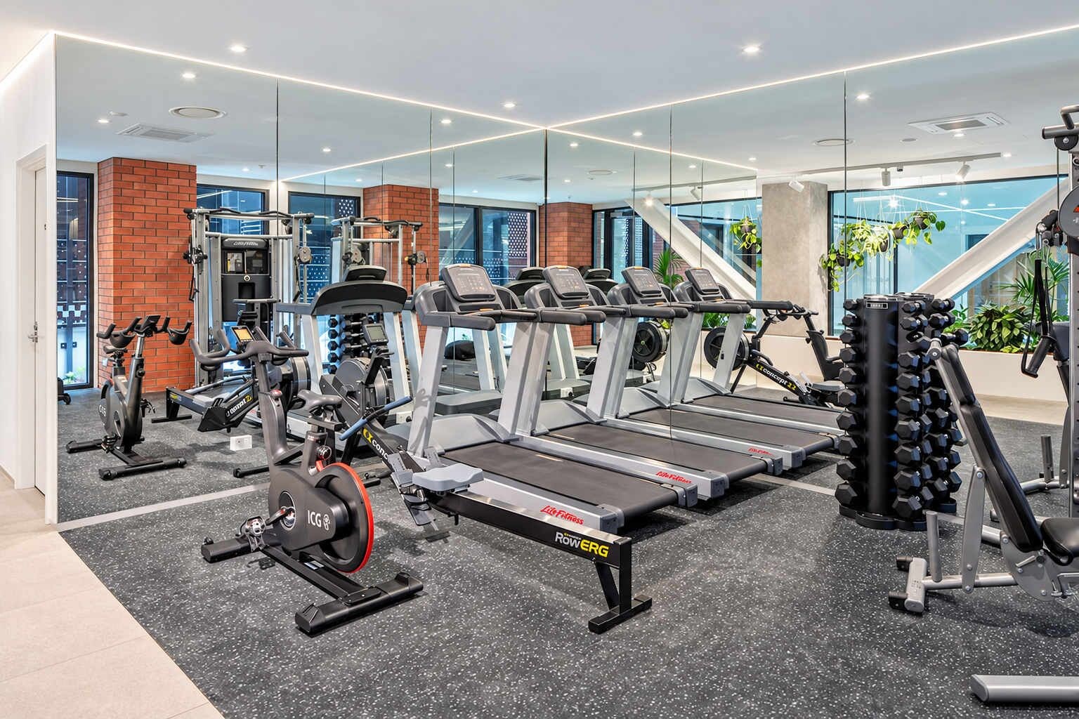 Une salle de sport moderne équipée de machines de cardio, de matériel de musculation et dotée d’un mur entièrement recouvert de miroirs.