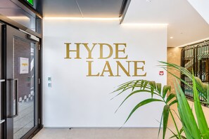 Entrada de un hotel con un letrero que dice 'HYDE LANE' en letras doradas sobre una pared blanca.