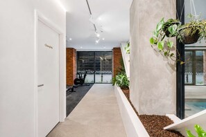 A hallway with a door labeled 'Changing,' a brick wall, a window with a view, and a hanging plant.