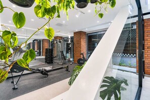 Une salle de sport équipée de matériel d’exercice, d’un rameur et d’un escalier menant à un balcon agrémenté de plantes.