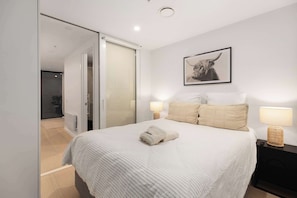 Une chambre à coucher avec un lit, deux lampes de chevet, un tableau encadré au mur et une porte donnant sur une salle de bain.