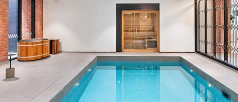 A modern indoor swimming pool with a clear blue water surface, surrounded by a tiled floor and a glass partition.