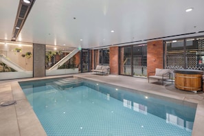 A modern indoor pool area with a clear pool, seating by the pool, and a staircase leading to an upper level.