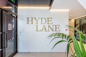 Siisti, moderni sisustus, seinällä huomiota herättävä kyltti, jossa lukee ”HYDE LANE”, lasiovet ja ruukussa oleva kasvi.