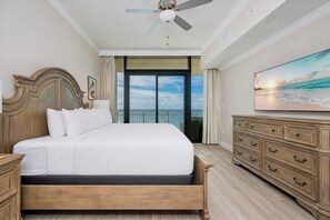 Ein Hotelzimmer mit einem Bett, einem Deckenventilator, einem großen Fenster mit Meerblick und einem Schminktisch.