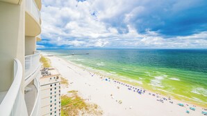 A beach view from a balcony with a pier in the distance.
