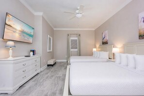 A hotel room with a large bed, a bedside table with a lamp, a dresser, a ceiling fan, and a painting on the wall.