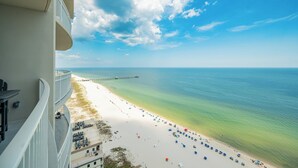 A beach view from a balcony with a clear sky, a sandy beach, and a pier in the distance.
