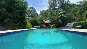 A clear blue swimming pool surrounded by lush greenery and a small building with a red roof.