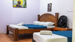 A single bed with a wooden headboard, a bedside table, a fan, and a blue blanket.