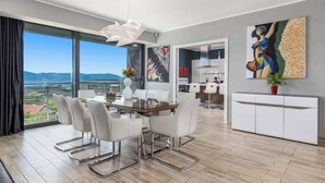 A modern dining area with a glass table and white chairs, a white cabinet, and a large abstract painting on the wall.