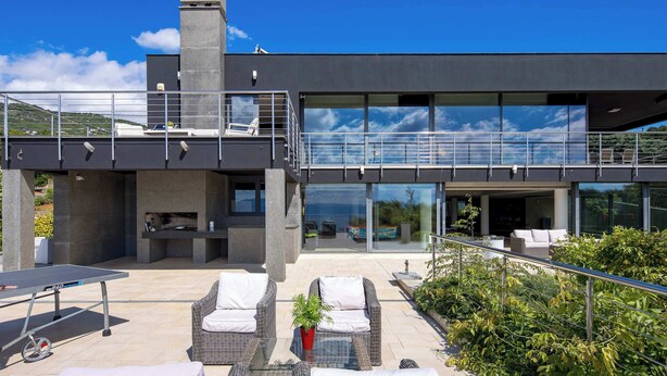 A modern outdoor patio with wicker furniture, a ping pong table, and a stone fireplace.
