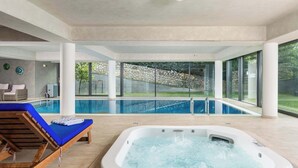 A modern indoor pool area with a hot tub, lounge chairs, and a view of the outdoor pool.