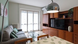 A modern living room with a sofa, a glass dining table, and a TV on a wooden cabinet. - notaMi - Feels Like Home (Milan)