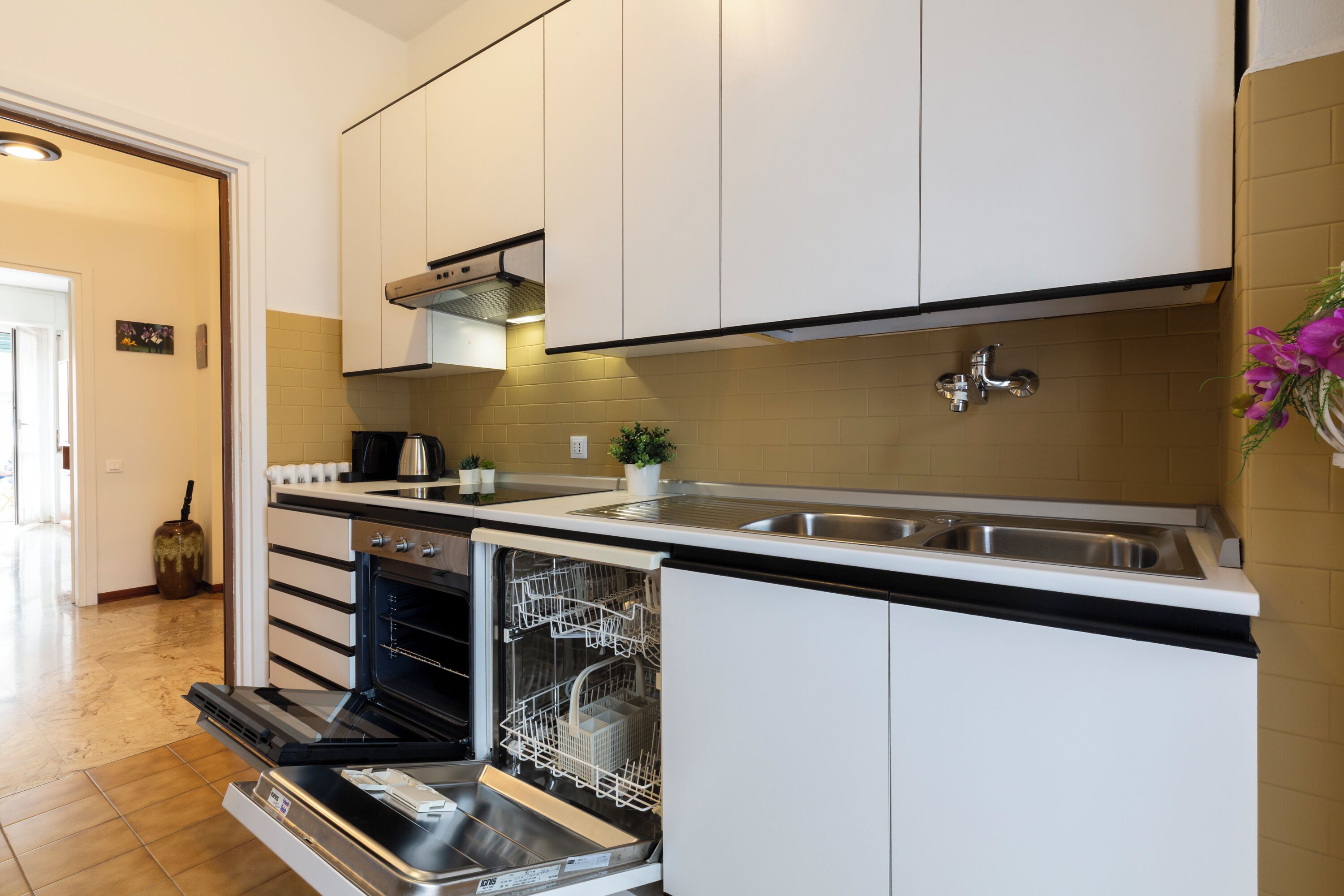 A modern kitchen with white cabinets, a built-in dishwasher, and a stainless steel sink.