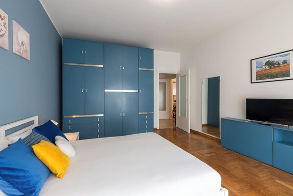 A bedroom with a bed, blue wardrobe, TV, and artwork on the wall. - notaMi - Feels Like Home (Milan)