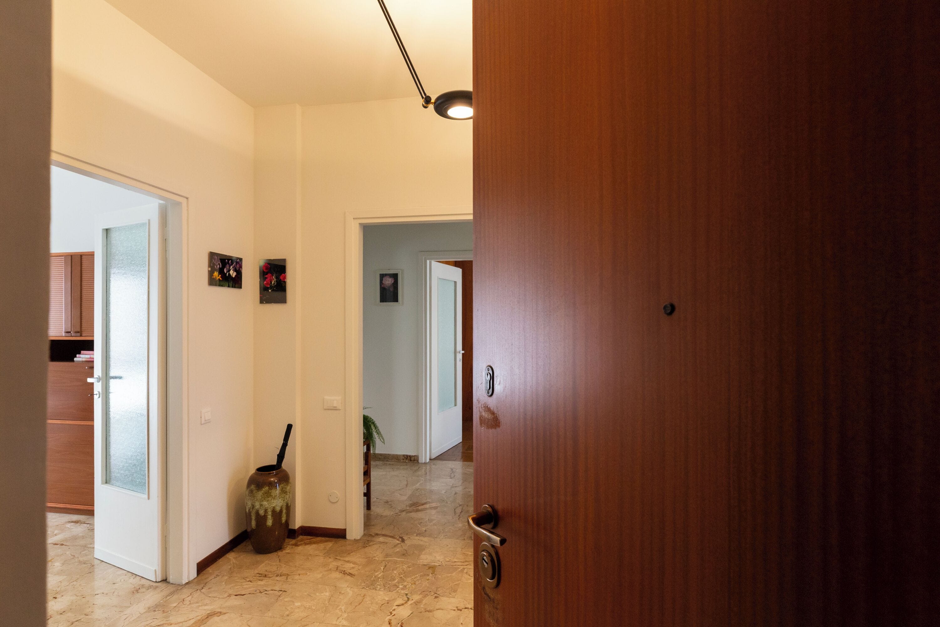Um corredor com porta de madeira, piso de mármore e um pequeno vaso com puxador preto.