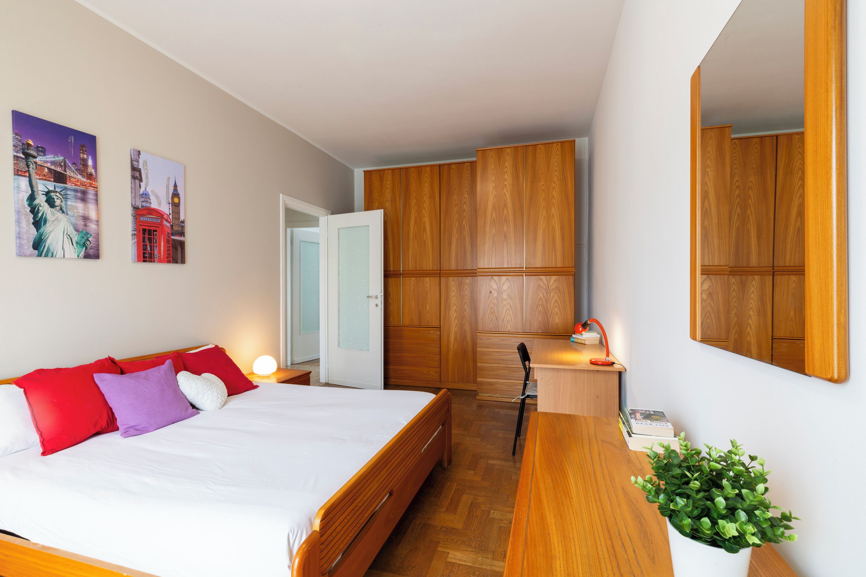 Une chambre à coucher comprenant un lit, une armoire en bois, une table de chevet, une lampe et une plante en pot.
