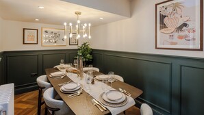 A dining area with a long wooden table set for a meal, framed artwork on the walls, and a chandelier above. - The Clifton Residence (Bristol)