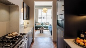 A modern kitchen with a built-in stove, a dining area with a sofa and a coffee table, and a view into a living room with a large window and a hanging light fixture. - The Clifton Residence (Bristol)