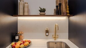 A kitchen with a white countertop, a stainless steel sink, a gold faucet, and a wooden shelf above the sink holding kitchen items. - The Clifton Residence (Bristol)