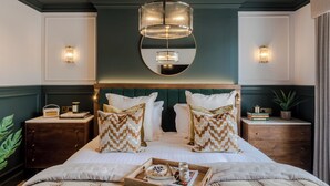 A bedroom with a large bed, two bedside tables, a mirror above the bed, and a chandelier. - The Clifton Residence (Bristol)